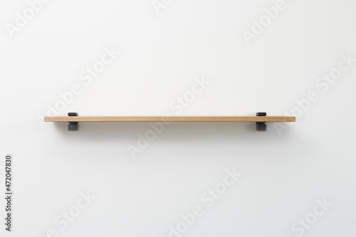 straight view of wooden shelf with black bracing over white wall background.