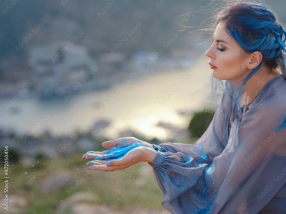 Φωτογραφία woman in dress against mountains and sea blows off blue sparkles.