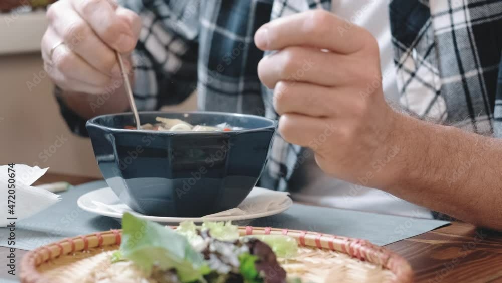 A man is stirring a ready-made noodle soup and seasonings in a plate while sitting in a restaurant. The concept of Vietnamese cuisine. Hands of a man in close-up. A man is stirring a ready-made noodle soup and seasonings in a plate while sitting in a restaurant. The concept of Vietnamese cuisine. Hands of a man in close-up.