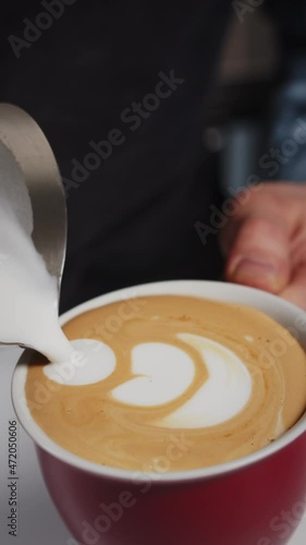 Barista making of cafe latte art with beautiful shape texture. Vertical video for smartpone and web purposes of barista hands pouring milk into coffee cup with cappuccino. Slow motion
