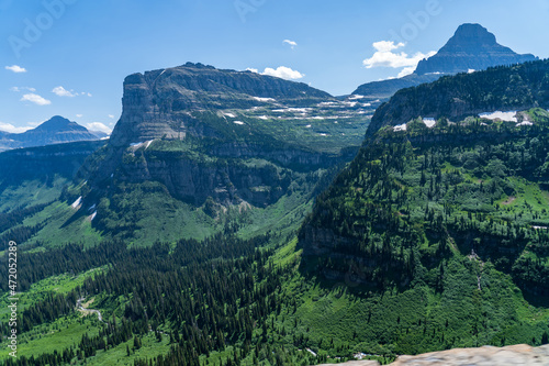 View from Logan Pass in Glacier National Park, Montana on a sunny summer day, with glacial valley, snow-capped mountains, alpine lakes, and grass