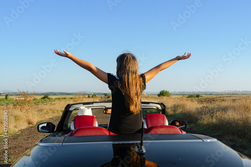 A child with outstretched arms sits in the back seat of a black cabriolet without a roof