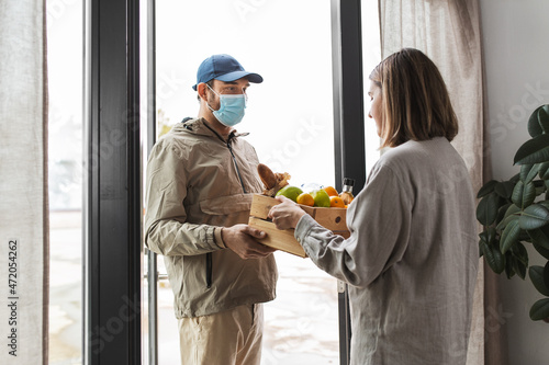 food shipping, pandemic and people concept - delivery man in mask giving order in wooden box to female customer at home