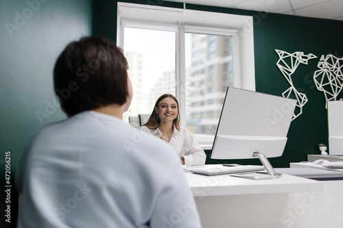 Smiling saleswoman talking to client at desk in travel agency photo