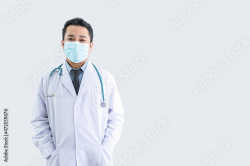 Smiling male doctor in lab clothes hand in pocket wearing a mask with white background