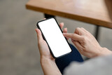 Woman sitting holding a smartphone blank white screen at café. Mock up