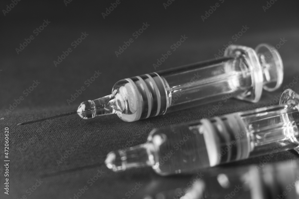 Close view of the glass syringes on a gray background. Medicine and health concept. Vaccine against viruses. Needle and drugs. Black and white Close view of the glass syringes on a gray background. Medicine and health concept. Vaccine against viruses. Needle and drugs. Black and white