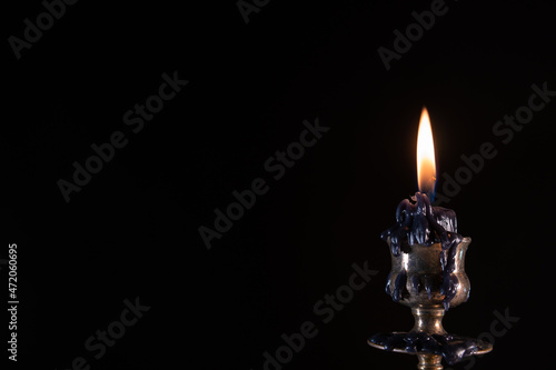 Burning black candle. Stands in an old brass metal candlestick. Black background. Vintage style concept, dramatic and mystic. Copy space