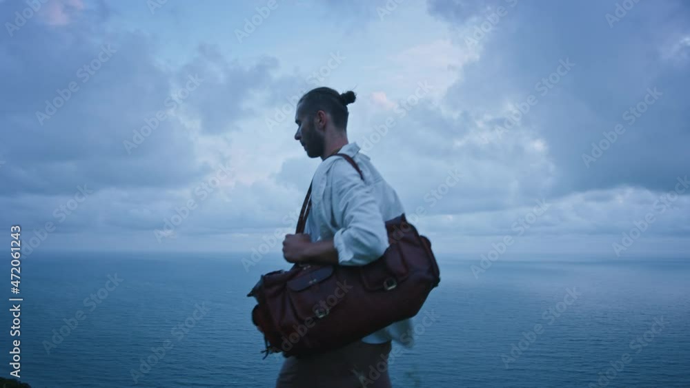 Brave young handsome stranger traveler man walk in beautiful wheat field in windy north mountain sea landscape, moody clouds with bag on his shoulder. Cinematic freedom people concept Brave young handsome stranger traveler man walk in beautiful wheat field in windy north mountain sea landscape, moody clouds with bag on his shoulder. Cinematic freedom people concept