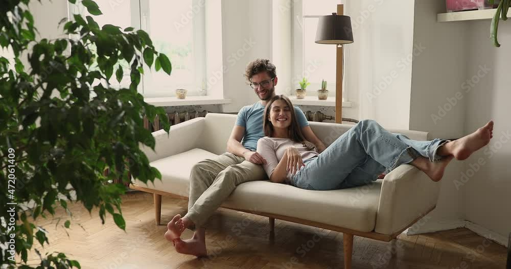 Peaceful serene young couple cuddle on soft cozy sofa at home talk chat smile share plans ideas on future. Affectionate millennial husband sit on couch embrace beloved wife enjoy pleasant conversation Peaceful serene young couple cuddle on soft cozy sofa at home talk chat smile share plans ideas on future. Affectionate millennial husband sit on couch embrace beloved wife enjoy pleasant conversation