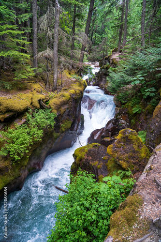 Clear turqoise water cascades over red rock waterfalls on Avalanche Creek in Glacier National Park on a summer day in Montana