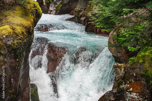 Clear turqoise water cascades over red rock waterfalls on Avalanche Creek in Glacier National Park on a summer day in Montana