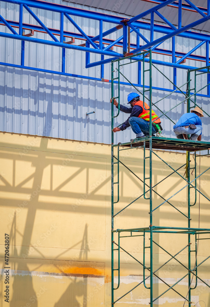 Two construction workers are installing high scaffolding for working on top of warehouse building structure in construction site