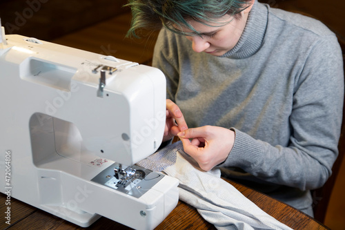 The girl sews while sitting at the sewing machine. Skill, hobby, profession.