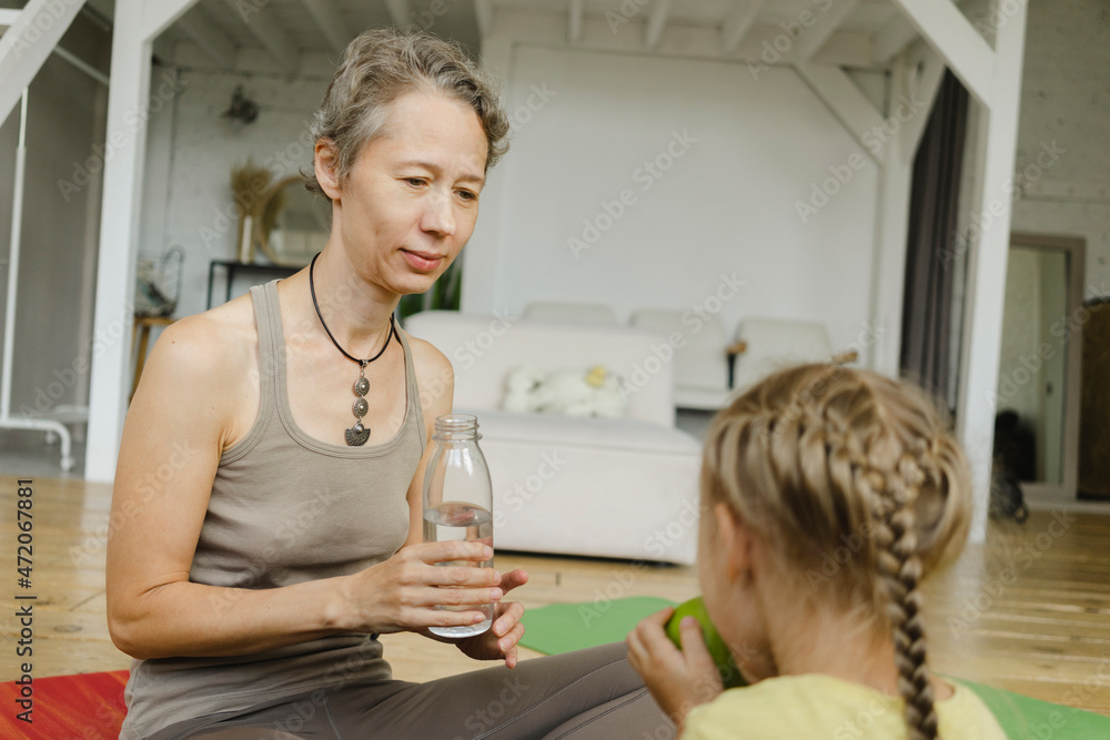 Mother looking at daughter eating fruit at home Mother looking at daughter eating fruit at home