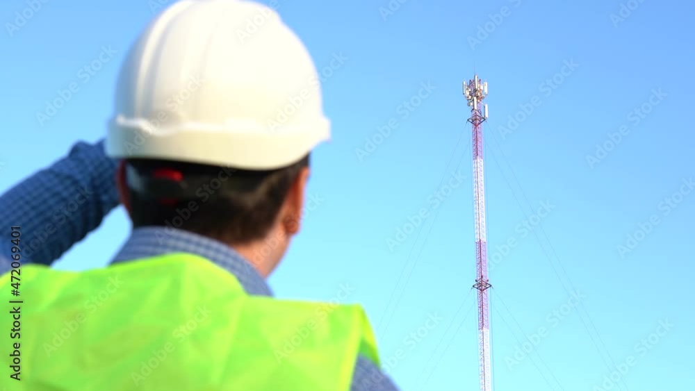An engineer photographs a telecom tower for a report. Back view An engineer photographs a telecom tower for a report. Back view