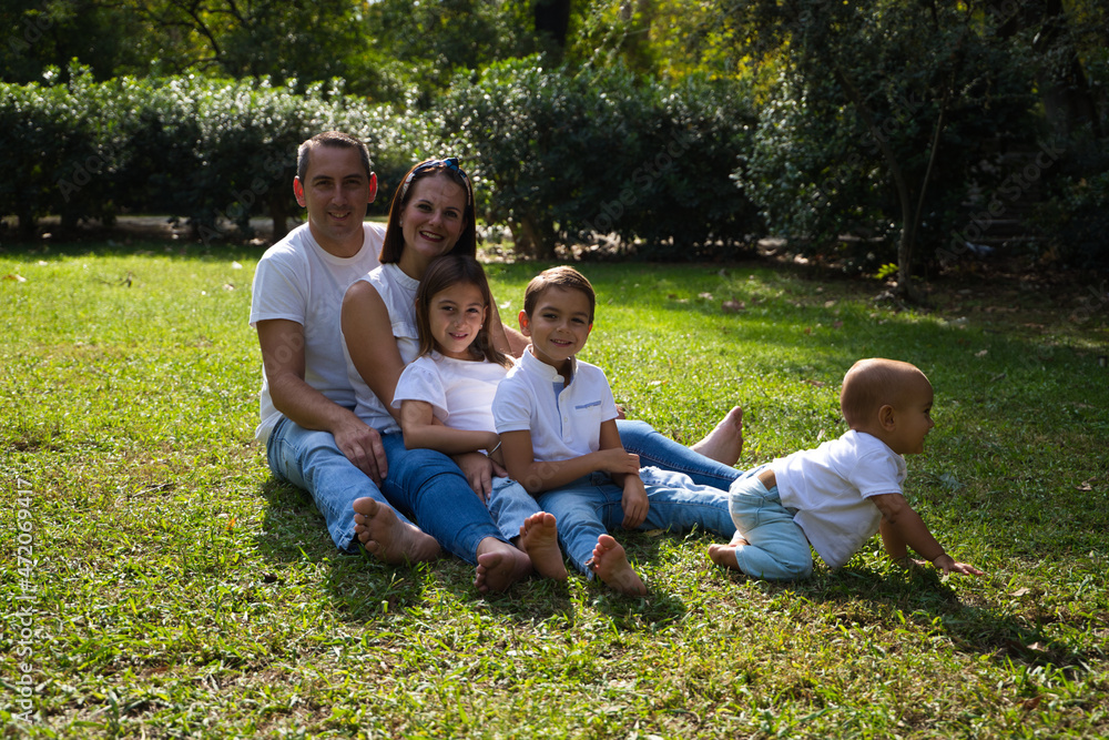 Fototapeta premium Portrait of happy parents with their three children lying in the park. The eldest daughter is a transgender girl. Concept of family happy united family with children.