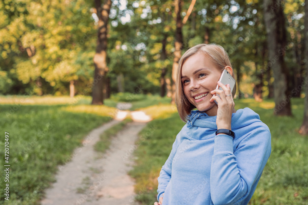 Cheerful young woman in hoodie talking on cellphone in forest Cheerful young woman in hoodie talking on cellphone in forest