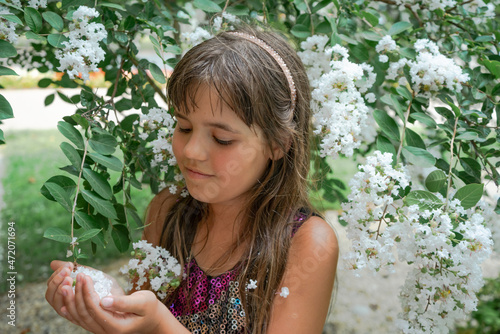 A girl with long hair in the park among trees, greenery and white flowers