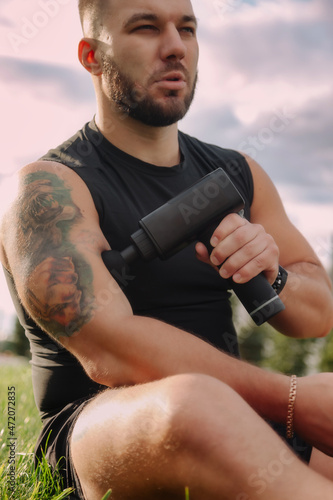 Fototapeta Naklejka Na Ścianę i Meble -  Man massages body with massage percussion gun device
