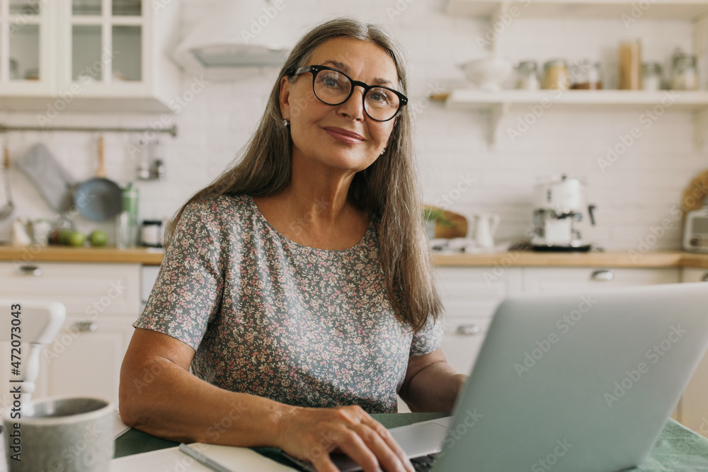Pretty middle-aged woman with grey hair working on her laptop sitting ...
