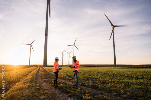 Engineer with digital tablet discussing with colleague at sunset