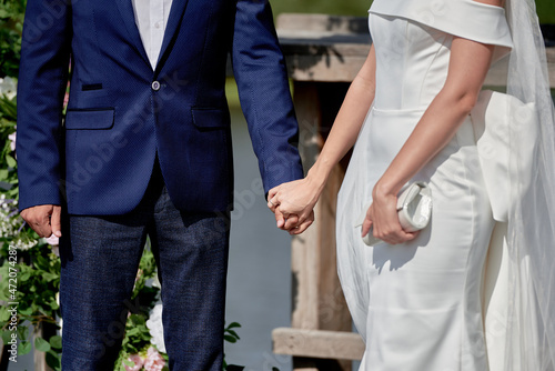 Happy bride and groom holding hands on wedding ceremony, copy space. Wedding couple in love, newlyweds. Bridal bouquet © mirage_studio