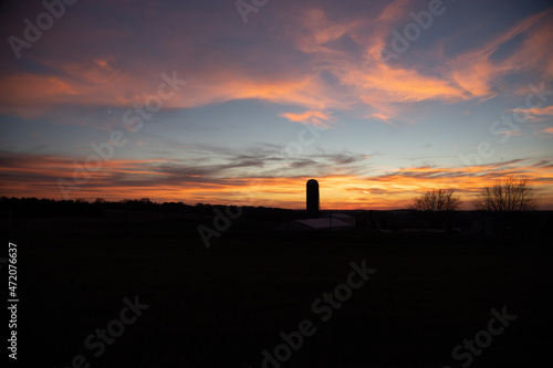 Sunset over a farm with a silo and a field