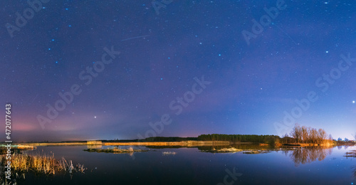 Belarus, Eastern Europe. Night Sky Stars Above Countryside Landscape With River. Natural Starry Sky Above Lake Pond In Early Spring Night. Russian Nature. Panorama, Panoramic View