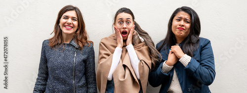 Horizontal banner or header Females looking at camera with isolated white wall on background. Each woman is doing a different facial expressions, one is happy, one is scared and one is sad