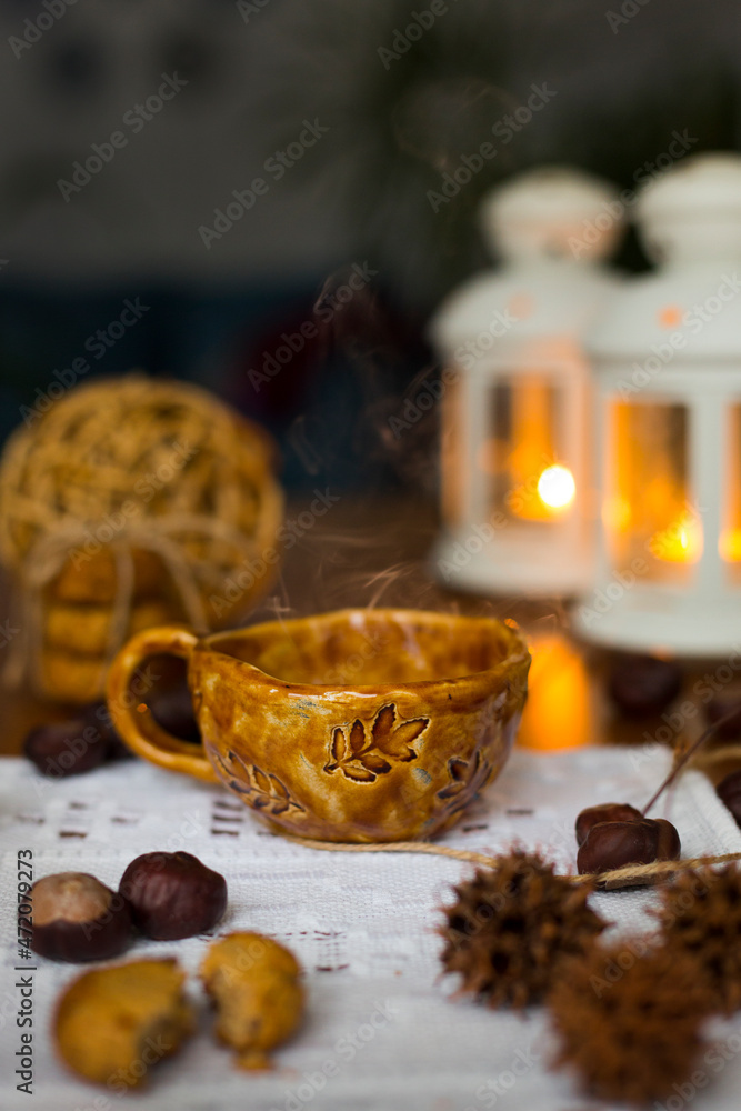 Cozy still life with red handmade pottery cup with hot tea with  steam over it against the background of candlesticks