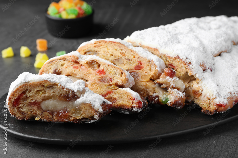Traditional Christmas Stollen with icing sugar on black table, closeup