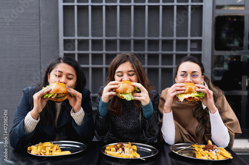 Females sitting at table restaurant biting burgers. Fast food unhealthy eating.
