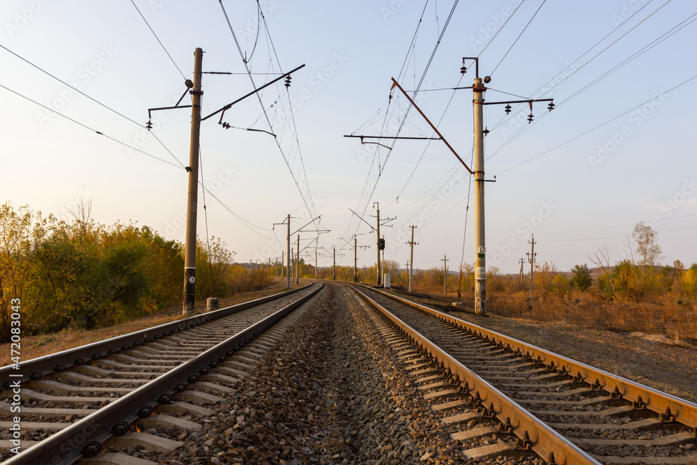 In the center there are parallel railway tracks and poles of electric wires extending into the distance at sunset