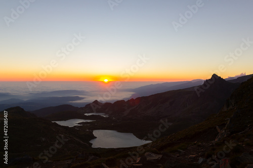 Sunrise in the mountains above the clouds on the top of the mountain overlooking the mountain lakes and mountains. The first rays of the sun on the horizon