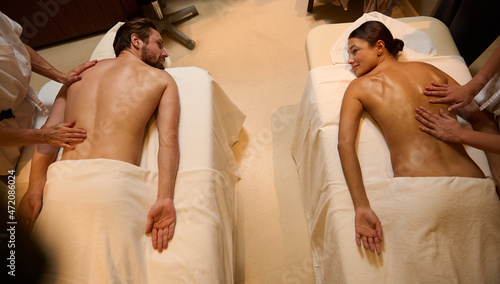 High angle view of adorable newlyweds, heterosexual couple getting body massage therapy at wellness clinic. Unrecognizable masseuses massaging the back muscles of a loving young cute couple