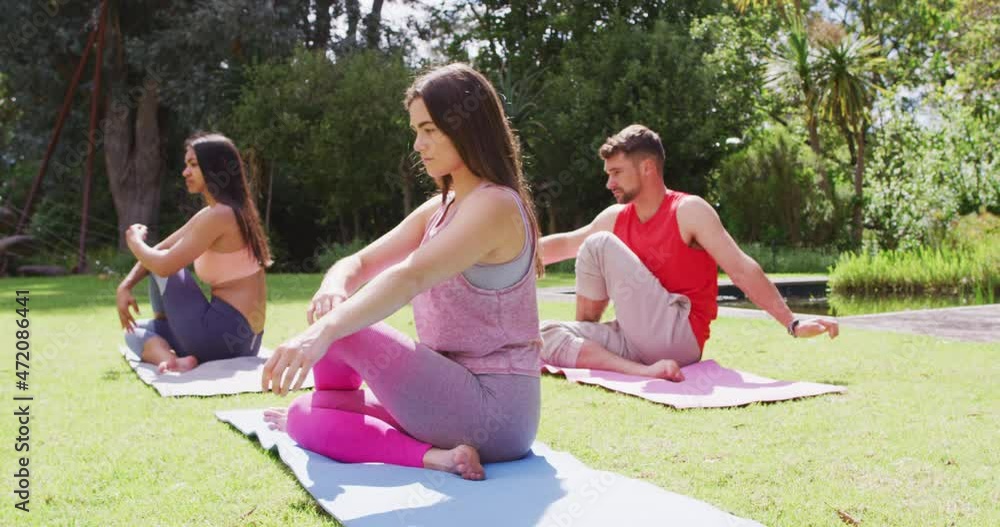Diverse group of men and women practicing yoga sitting on mats in sunny park Diverse group of men and women practicing yoga sitting on mats in sunny park