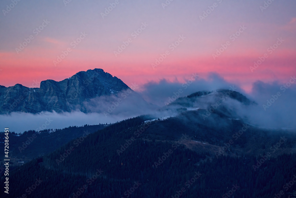breathtaking sunset at a cold autumn evening on the mountains with view of the alps witha pink sky and fog in the valley