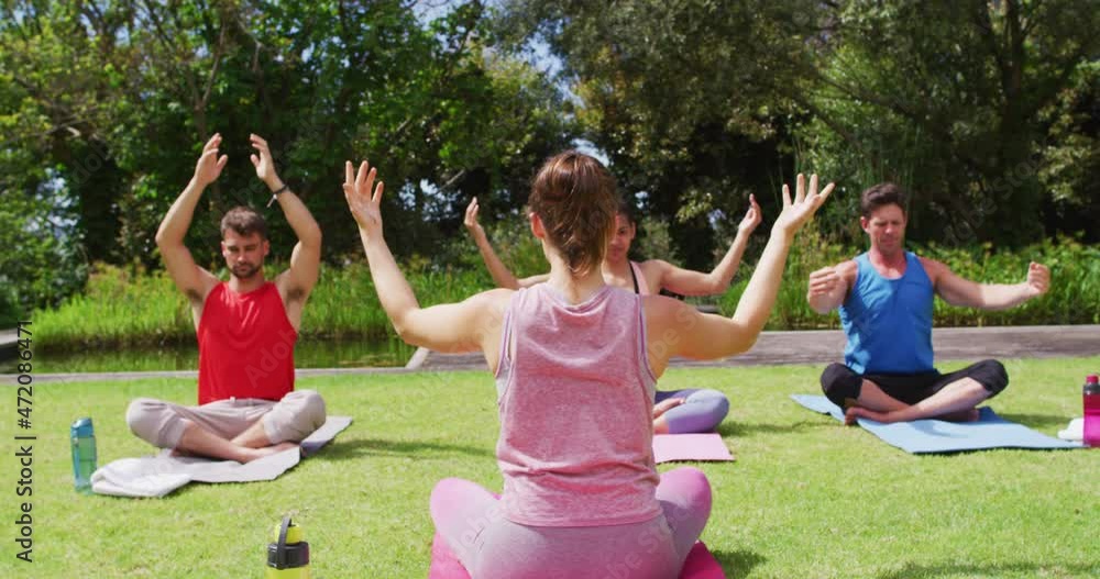 Rear view of caucasian female instructor practicing yoga with diverse group in park Rear view of caucasian female instructor practicing yoga with diverse group in park