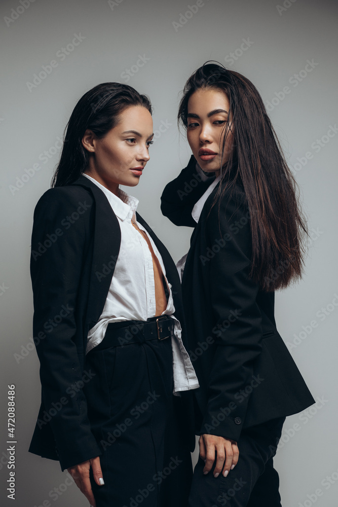 Two young women pose in studio standing in black suits. Two young women pose in studio standing in black suits.