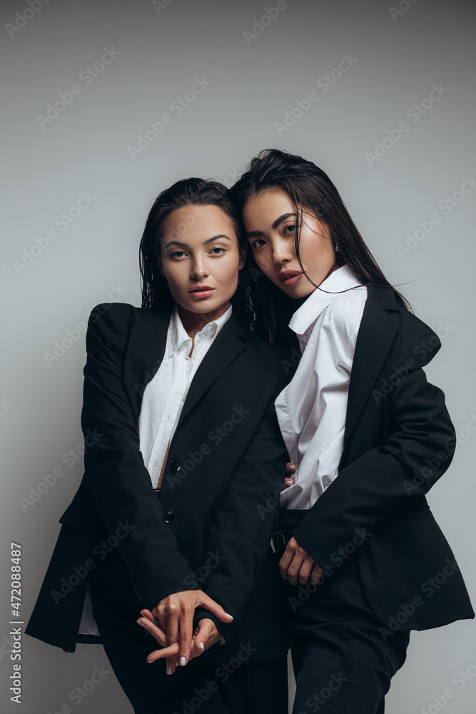 Two young women pose in studio standing in black suits. Two young women pose in studio standing in black suits.