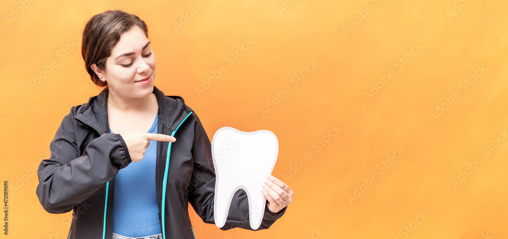 Girl pointing to a tooth shape, isolated over orange background. Girl pointing to a tooth shape, isolated over orange background.