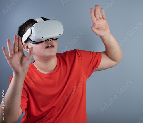 A young guy with Viar glasses. A teenager in a red T-shirt plays with white virtual reality glasses, looks with interest at something above, raised his hand up to touch