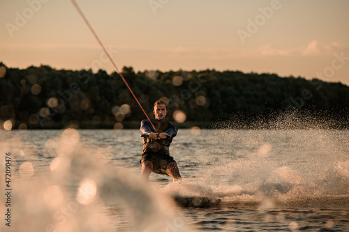 amazing view of attractive man holding rope and energetically riding wakeboard on splashing river wave.