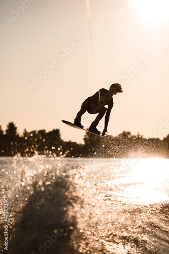 Beautiful silhouette of female rider holding rope and making jump on wakeboard. Water sports activity. photo