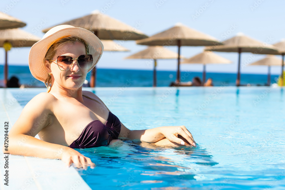 Young woman relaxing in swimming pool on summer vacation. Blonde, caucasian.