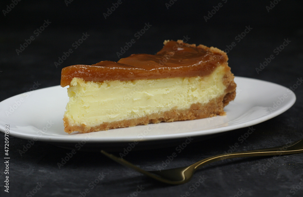 A piece of cheesecake is on the plate. There is a golden fork nearby. Concrete background.