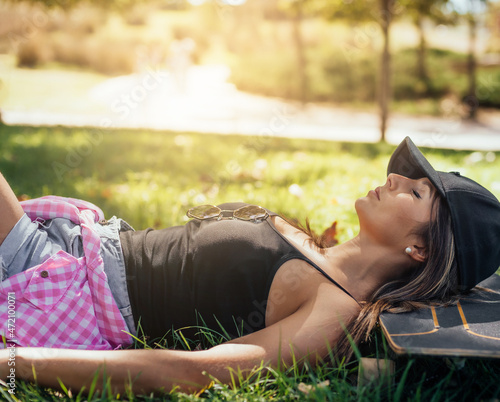 a caucasian girl lying on the grass, resting after skating. she is relaxed. concept of tranquility and rest in the open air.
