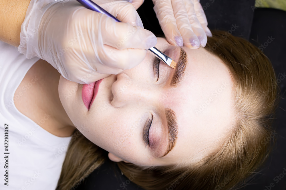 close-up of the model's face, the master applies a toning cream under the eyebrow after the lamination procedure close-up of the model's face, the master applies a toning cream under the eyebrow after the lamination procedure