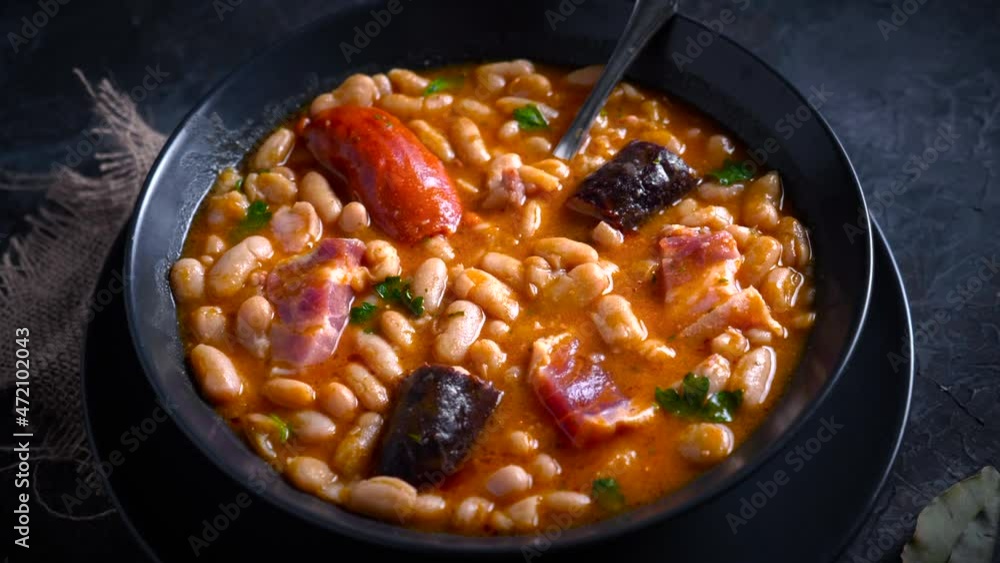 Traditional recipe of beans with chorizo and blood sausage called “Fabada Asturiana” on a dark table with some ingredients around. Typical Spanish food with “compango”. Traditional recipe of beans with chorizo and blood sausage called “Fabada Asturiana” on a dark table with some ingredients around. Typical Spanish food with “compango”.